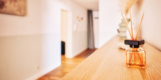Ein Flur mit Holzboden, links ein Bild an der Wand, rechts ein Tisch mit einem Duftdiffusor und getrockneten Gr&auml;sern.