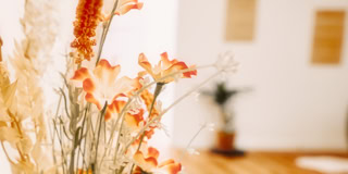 Ein Strau&szlig; aus getrockneten Blumen mit orangefarbenen und beigen T&ouml;nen, unscharfer Hintergrund mit Holzboden und Wanddekorationen.