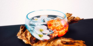 Eine Glasschale mit Wasser und schwimmenden Blumen, platziert auf einem St&uuml;ck Holz.