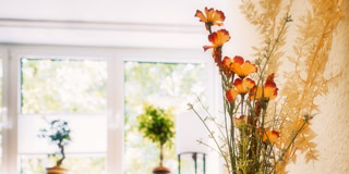 Ein Blumenstrau&szlig; mit orangefarbenen Blumen steht vor einem Fenster mit Blick auf B&auml;ume im Hintergrund.